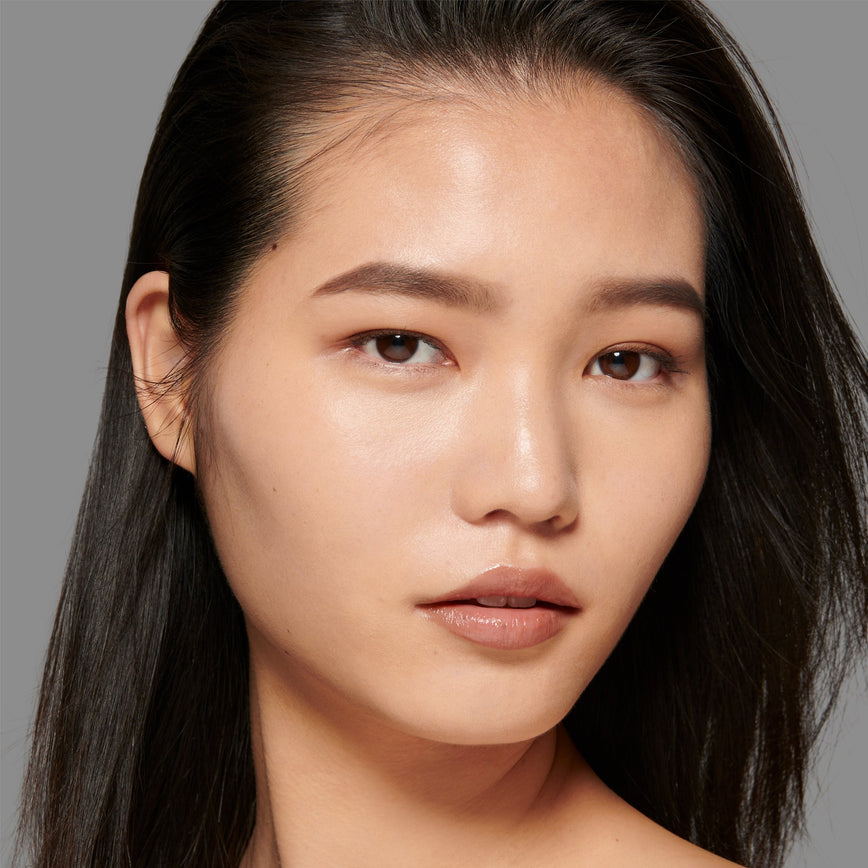 Lisa Eldridge Seamless Skin Foundation Pictured on Model. A young model with light skin and peach undertones, brown eyes and straight black hair.
