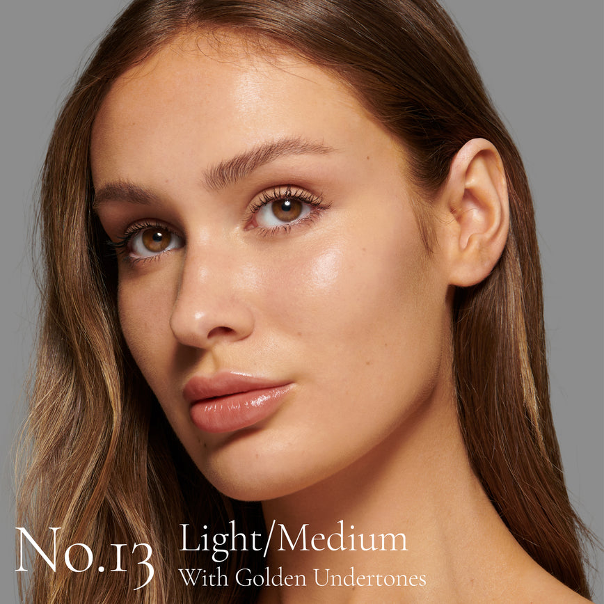 Lisa Eldridge Seamless Skin Foundation Pictured on Model. The model has light/medium skin and golden undertones, brown eyes and straight brown hair. The text says ‘No.13 Light/Medium With Golden Undertones’