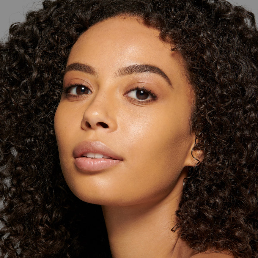 Lisa Eldridge Seamless Skin Foundation Pictured on Model. The model has medium skin and golden undertones, brown eyes and curly black hair.
