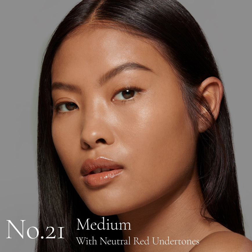 Lisa Eldridge Seamless Skin Foundation Pictured on Model. The model has medium skin and neutral red undertones, brown eyes and straight black hair. The text says ‘No.21 Medium With Neutral Red Undertones’