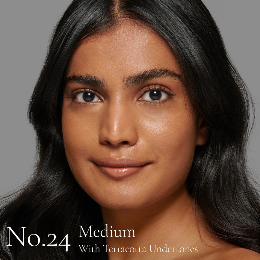 Lisa Eldridge Seamless Skin Foundation Pictured on Model. The model has medium skin and golden terracotta undertones, brown eyes and wavy black hair. The text says ‘No.24 Medium With Terracotta Undertones’