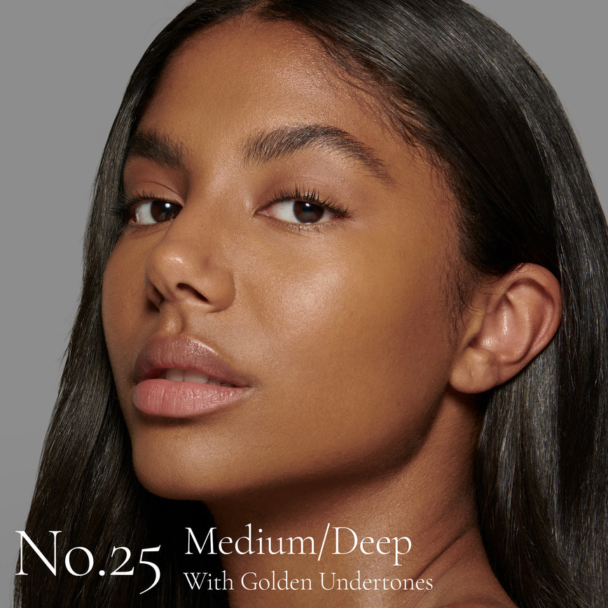 Lisa Eldridge Seamless Skin Foundation Pictured on Model. The model has medium/deep skin and golden undertones, brown eyes and straight black hair. The text says ‘No.25 Medium/Deep With Golden Undertones’