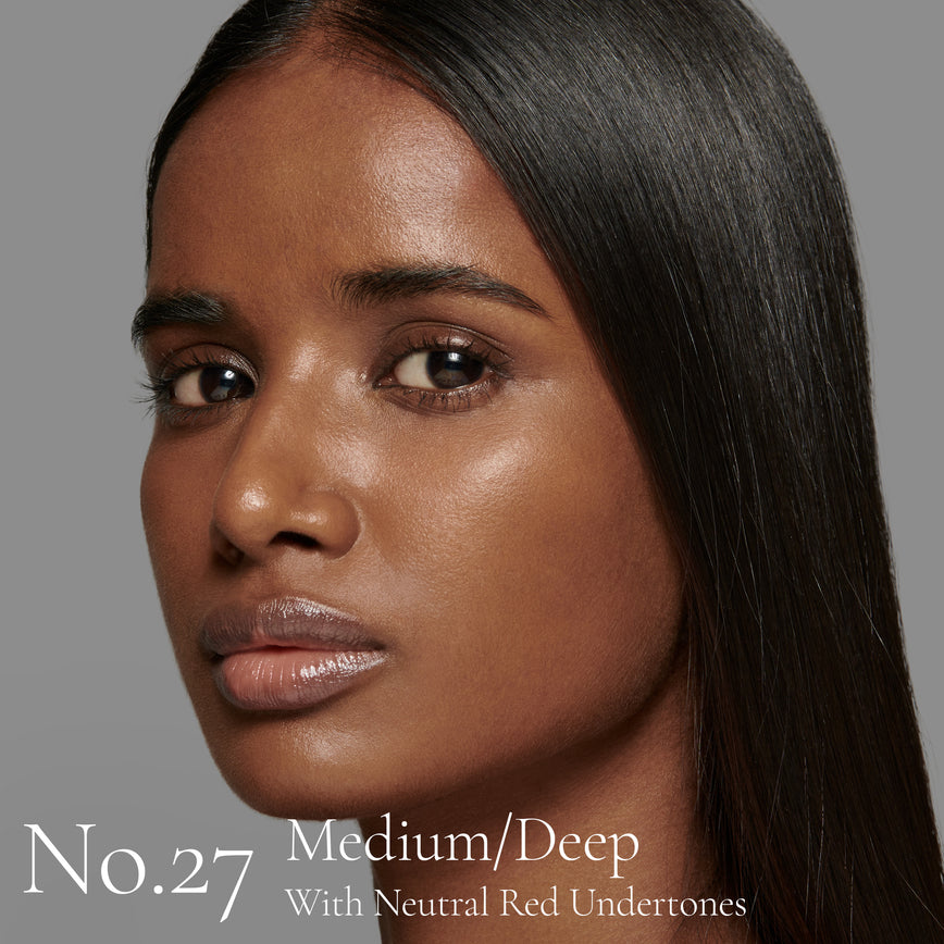 Lisa Eldridge Seamless Skin Foundation Pictured on Model. The model has medium/deep skin and neutral red undertones, brown eyes and straight black hair. The text says ‘No.27 Medium/Deep With Neutral Red Undertones’