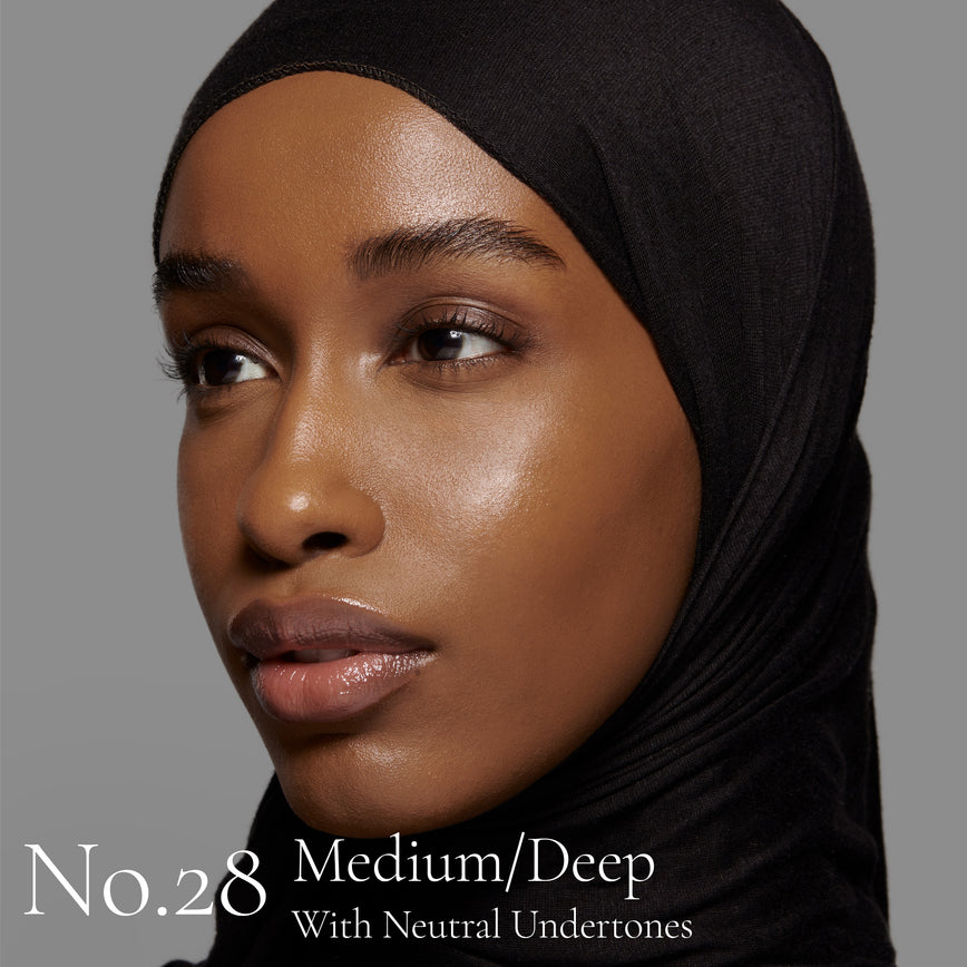 Lisa Eldridge Seamless Skin Foundation Pictured on Model. The model has medium/deep skin and neutral undertones, brown eyes and wears a black headscarf. The text says ‘No.28 Medium/Deep With Neutral Undertones’