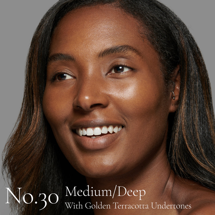 Lisa Eldridge Seamless Skin Foundation pictured on model. The model has medium/deep skin and golden terracotta undertones, brown eyes and black hair with auburn highlights. The text says ‘No.30 Medium/Deep With Golden Terracotta Undertones’