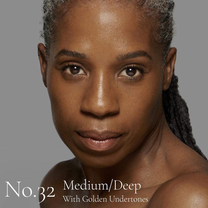 Lisa Eldridge Seamless Skin Foundation pictured on model. The model has medium/deep skin and golden undertones, brown eyes and black and grey hair. The text says ‘No.32 Medium/Deep With Golden Undertones’