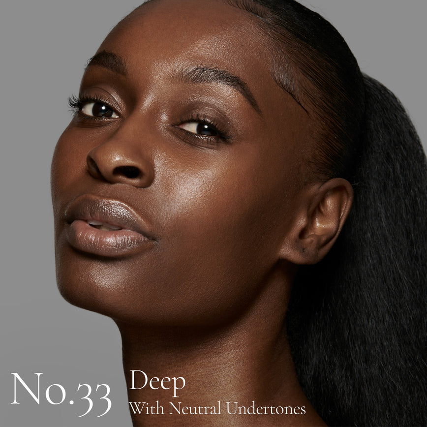 Lisa Eldridge Seamless Skin Foundation pictured on model. The model has deep skin and neutral undertones, brown eyes and black hair. The text says ‘No.33 Deep With Neutral Undertones’