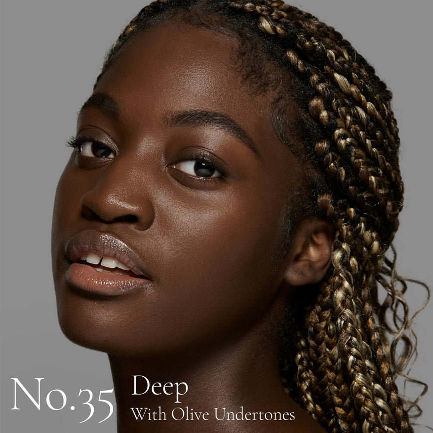 Lisa Eldridge Seamless Skin Foundation pictured on model. The model has deep skin and olive undertones, brown eyes and black hair with blonde highlights. The text says ‘No.35 Deep With Olive Undertones’