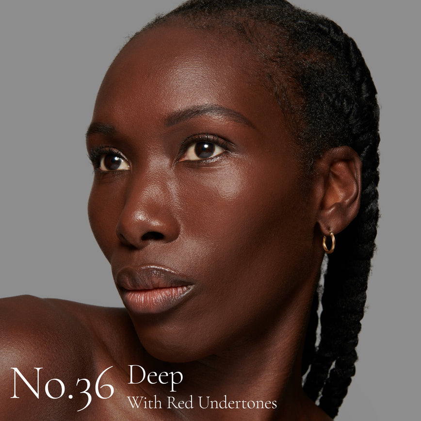 Lisa Eldridge Seamless Skin Foundation pictured on model. The model has deep skin and red undertones, brown eyes and black hair. The text says ‘No.36 Deep With Red Undertones’