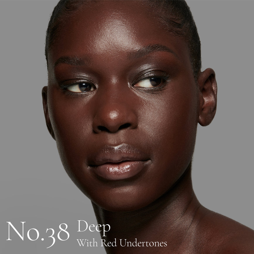 Lisa Eldridge Seamless Skin Foundation pictured on model. The model has deep skin and red undertones, brown eyes and black hair. The text says ‘No.38 Deep With Red Undertones’