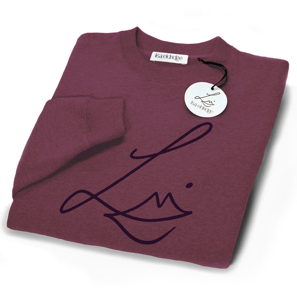 The Lisa Eldridge Studio Sweatshirt in velvet midnight folded up. The crewneck and the cuffs have a fine rib. The Lisa Eldridge logo is large on the front. There is a label that says “lisa eldridge’ sewn on the inside. Attached to the size label is a circular card tag on a black ribbon with the Lisa Eldridge logo in gold